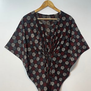 May include: A black, red, and white patterned kaftan with a V-neck and short sleeves. The kaftan has a tie at the waist.
