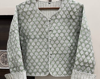 May include: A green quilted jacket with a white floral print. The jacket has a V-neck and long sleeves with striped cuffs.