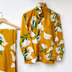 May include: A yellow and white pajama set with green leaf print. The set includes a long-sleeved shirt with a button-up front and matching pants.