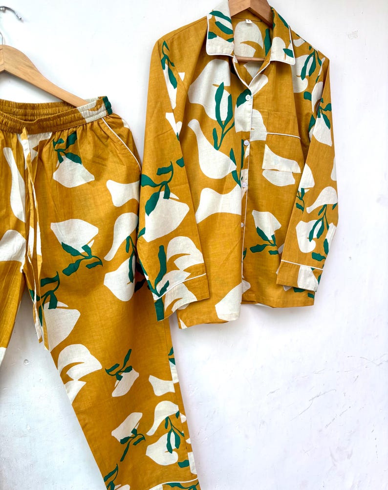 Puede incluir: Un conjunto de pijama amarillo mostaza y blanco con estampado floral. La parte superior tiene mangas largas y un cierre de botones en la parte delantera. Los pantalones tienen una cintura con cord&oacute;n.