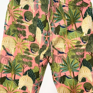 May include: Pink pants with a peacock and garden print. The pants have an elastic waistband and a drawstring.