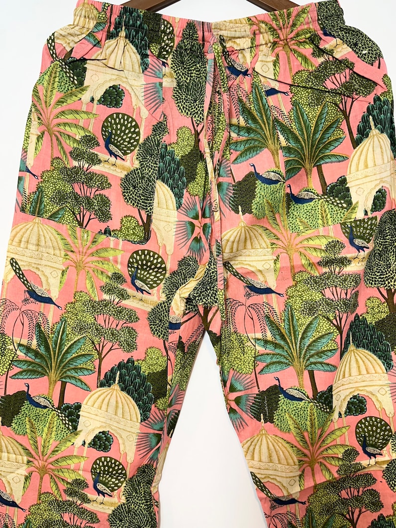 May include: Pink pants with a peacock and garden print. The pants have an elastic waistband and a drawstring.