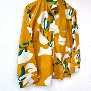 Puede incluir: Una camisa de manga larga de color amarillo mostaza con un estampado floral abstracto blanco y verde. La camisa tiene un cierre de botones en la parte delantera y un cuello.