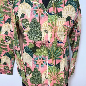May include: A pink pajama top with a white trim and a print of peacocks, palm trees, and white buildings.