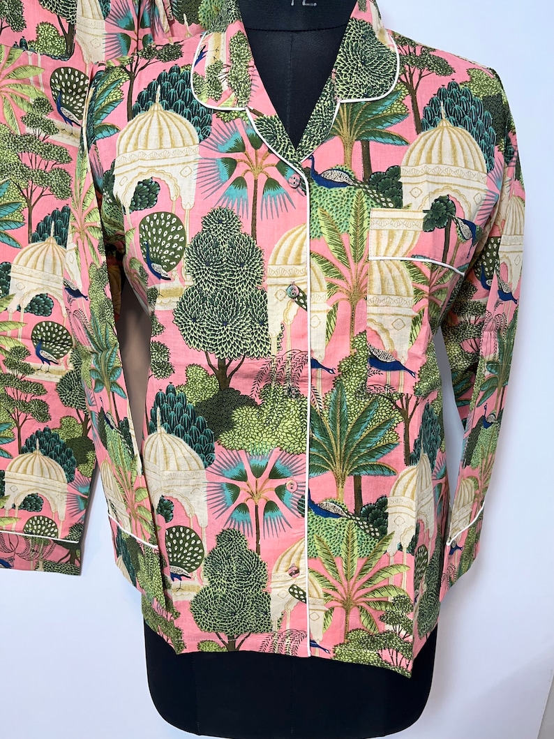 May include: A pink pajama top with a white trim and a print of peacocks, palm trees, and white buildings.