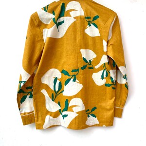 Puede incluir: Una camisa de manga larga con fondo amarillo mostaza y estampado floral blanco y verde.