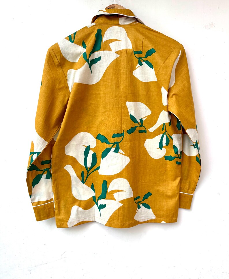 Puede incluir: Una camisa de manga larga con fondo amarillo mostaza y estampado floral blanco y verde.