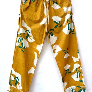 Puede incluir: Pantal&oacute;n amarillo mostaza con estampado floral blanco y verde. El pantal&oacute;n tiene una cintura el&aacute;stica y un cord&oacute;n.