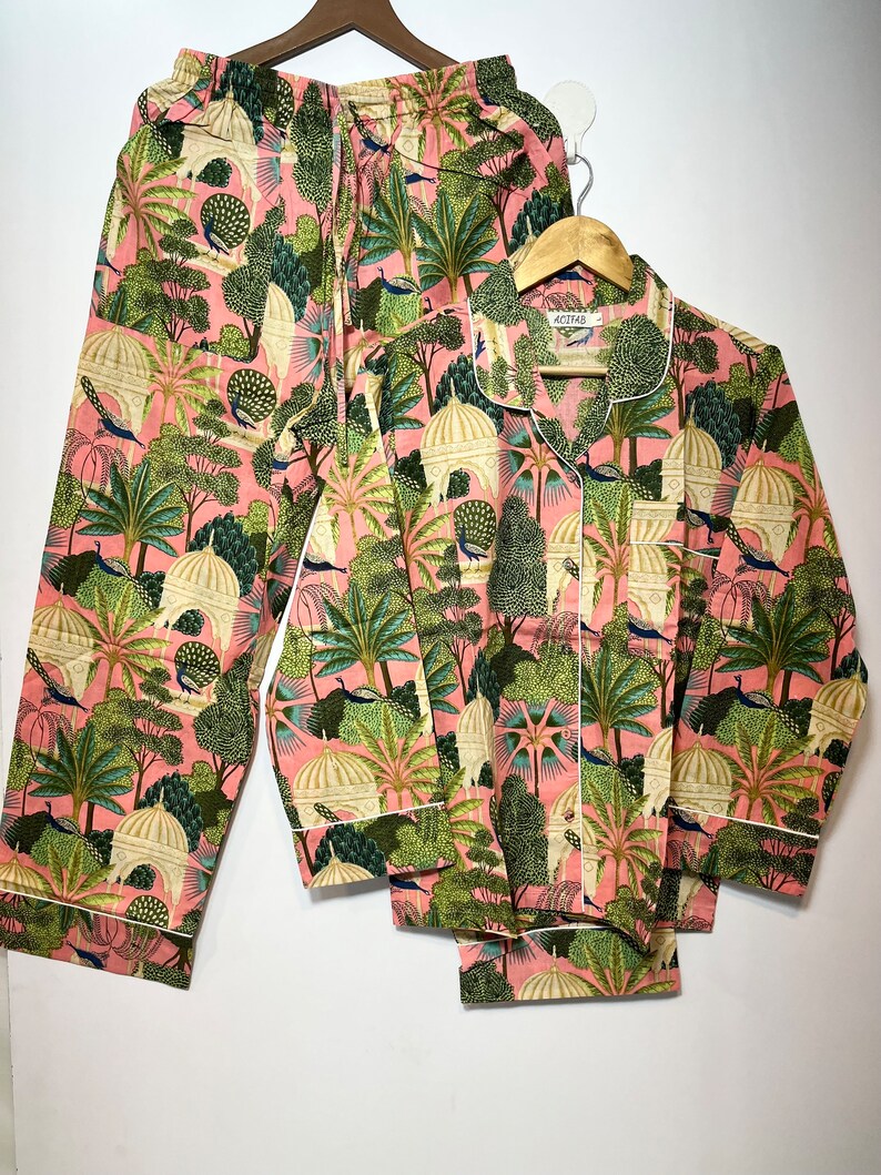 May include: A pink pajama set with a green and white print of peacocks, trees, and domes. The set includes a long-sleeved shirt with a button-up front and matching pants.