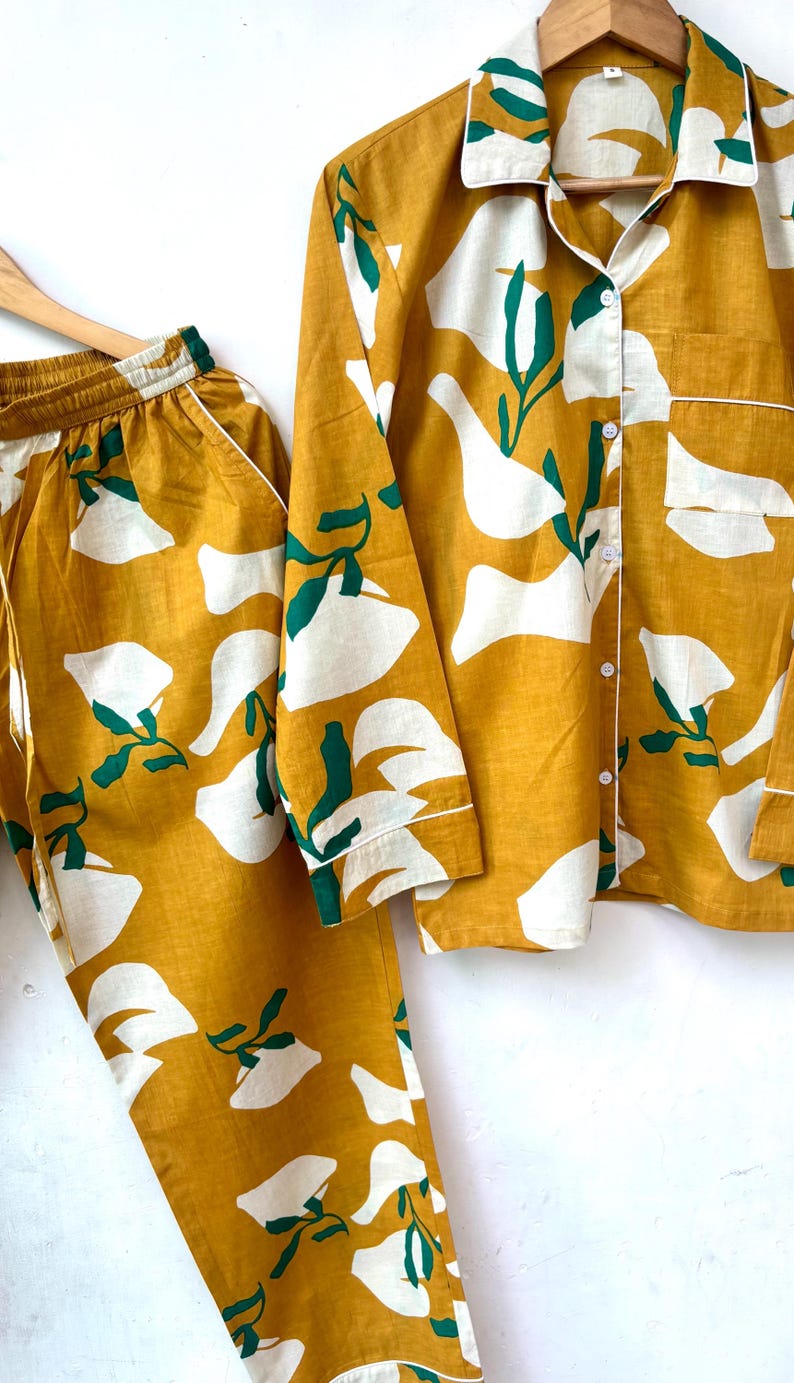 Puede incluir: Un conjunto de pijama amarillo mostaza con estampado floral abstracto blanco y verde. La parte superior tiene mangas largas y cierre de botones en la parte delantera. El pantal&oacute;n tiene una cintura el&aacute;stica.