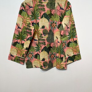 May include: A pink long-sleeved shirt with a white trim. The shirt features a repeating pattern of peacocks, trees, and domed buildings in shades of green, white, and cream.