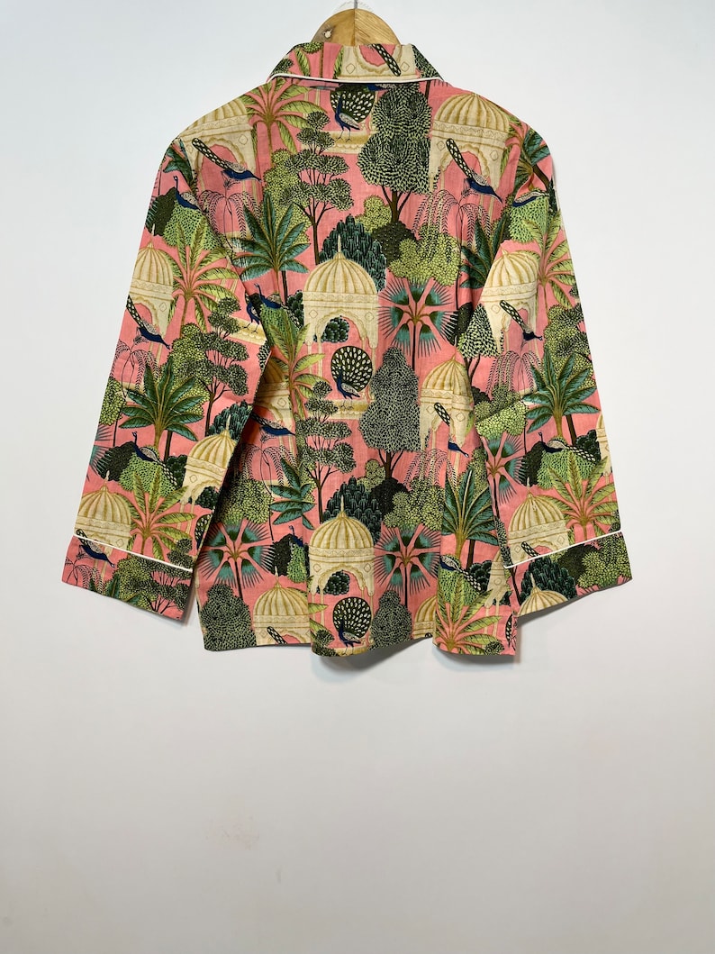 May include: A pink long-sleeved shirt with a white trim. The shirt features a repeating pattern of peacocks, trees, and domed buildings in shades of green, white, and cream.