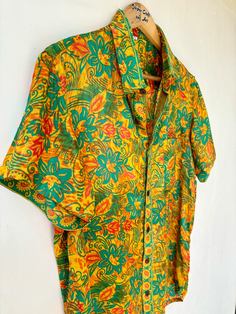 May include: A short-sleeved button-down shirt with a floral print in shades of yellow, green, and orange. The shirt has a pocket on the left side and a label that reads "Jaipur Craft and Art".