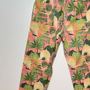 May include: Pink pajama pants with a white and green print of peacocks, trees, and buildings.