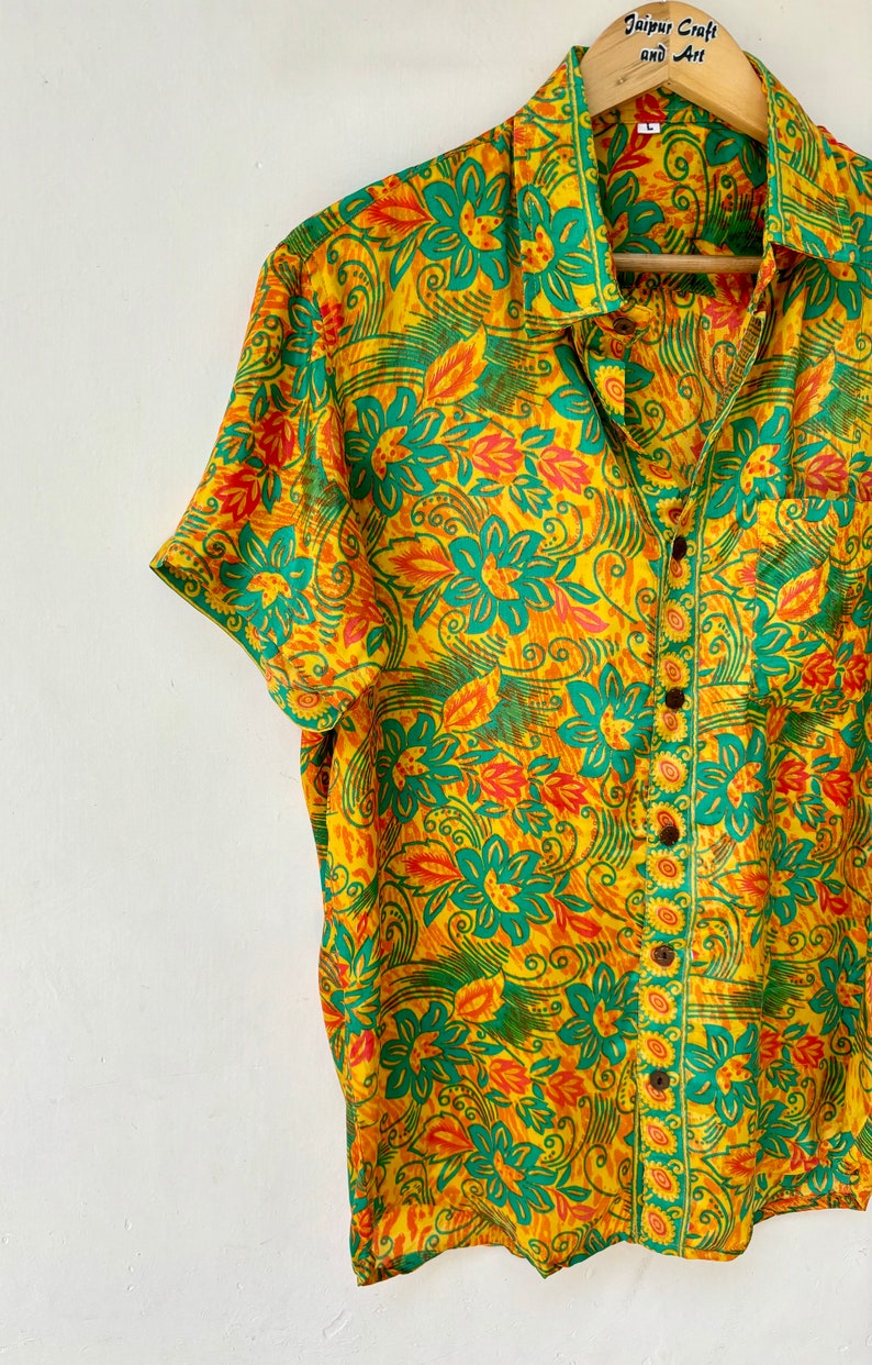 May include: A yellow, green and orange short-sleeved button-down shirt with a floral print. The shirt has a pocket on the left side and a button closure.