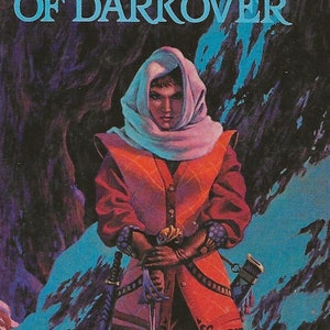 May include: A book cover featuring a woman in a red and white outfit holding a sword. The title of the book is "Free Amazons of Darkover" by Marion Zimmer Bradley.