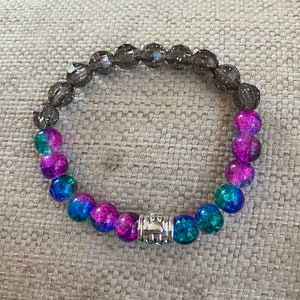 May include: A bracelet made of dark gray, pink, and blue glass beads with a silver charm in the center.