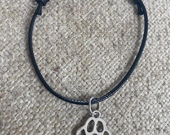 Puede incluir: Un brazalete de cuerda negro con un dije de huella de pata de plata.