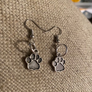 May include: A pair of silver dangle earrings with paw print charms. The earrings have a simple hook closure.