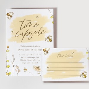 May include: A white card with a yellow watercolour background and the text "time capsule" in brown cursive. The card has instructions to be opened when Olivia turns 18 in 2027 and to leave a prediction or sweet message for Olivia. A smaller white card with a yellow watercolour background and the text "Dear Olivia," is also included.