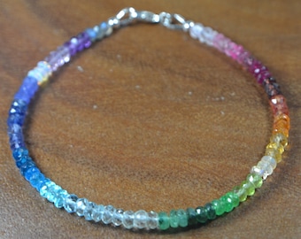 May include: A colorful beaded bracelet with a rainbow gradient of gemstones. The bracelet features a variety of colors, including blue, green, yellow, orange, pink, and purple. The bracelet is secured with a silver clasp.