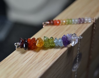 Può includere: Primo piano di due collane con pietre preziose color arcobaleno. Le pietre, dal rosso scuro al trasparente, sono disposte in fila. Le collane sono su una superficie di legno.