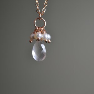 Puede incluir: Collar de oro rosa con un colgante de l&aacute;grima de cuarzo transparente facetado. El colgante est&aacute; adornado con peque&ntilde;as perlas y cuentas de oro rosa. La cadena es fina y tambi&eacute;n de oro rosa. El fondo es gris neutro.