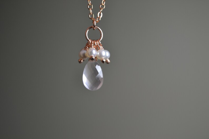 Puede incluir: Collar de oro rosa con un colgante de l&aacute;grima de cuarzo transparente facetado. El colgante est&aacute; adornado con peque&ntilde;as perlas y cuentas de oro rosa. La cadena es fina y tambi&eacute;n de oro rosa. El fondo es gris neutro.