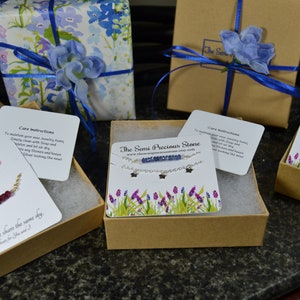 May include: An assortment of jewelry items, including necklaces and rings, presented in gift boxes. Some boxes are wrapped in floral paper and tied with blue ribbon. Each box contains a card with care instructions and the shop's name.