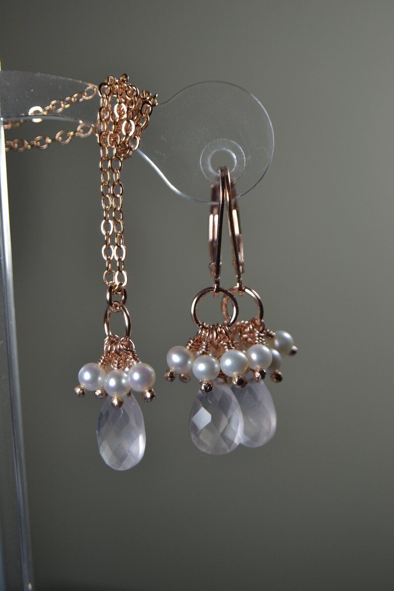 Puede incluir: Juego de joyas de oro rosa con collar y pendientes. El collar tiene una cadena fina con racimos de perlas y una gema rosa facetada en forma de l&aacute;grima. Los pendientes reflejan el dise&ntilde;o, con racimos de perlas y l&aacute;grimas rosas.