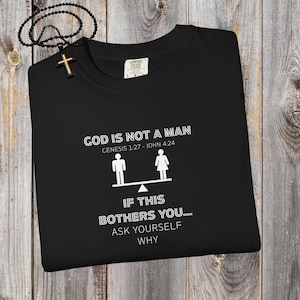 May include: Black t-shirt with white text: "GOD IS NOT A MAN" and "IF THIS BOTHERS YOU... ASK YOURSELF WHY". The shirt also features a graphic of a scale with a male and female figure. A black beaded necklace with a cross is in the image.