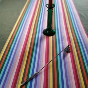 May include: A rainbow striped table runner with a green glass candle holder and a silver candle snuffer.