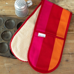 May include: Red and orange striped oven mitt with a white terrycloth lining. The mitt has a pocket with the text "Maison Elodie" printed on it.