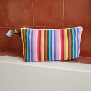 large rainbow wash bag on the edge of a bath with a red wall background