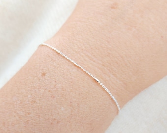 May include: A delicate silver chain bracelet featuring small, evenly spaced cylindrical metal beads along the length of the chain. The bracelet is thin and minimalist in its construction, resting against the skin with a subtle, reflective metallic finish.