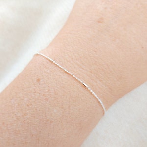 May include: A delicate silver chain bracelet with small, evenly spaced, rectangular accents.