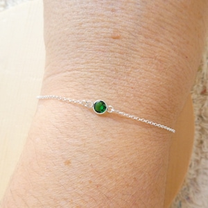 Op de afbeelding: Een delicate zilveren kettingarmband met een enkele groene edelsteen.