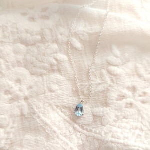 May include: A delicate silver chain necklace with a teardrop-shaped light blue gemstone pendant.