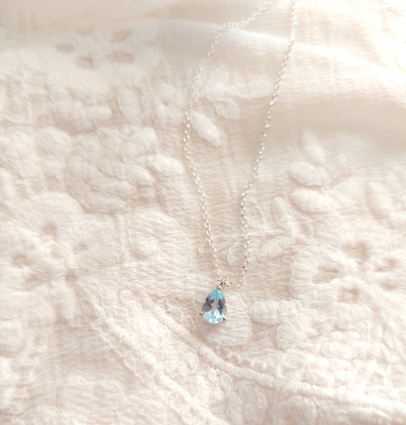May include: A delicate silver chain necklace with a teardrop-shaped light blue gemstone pendant.