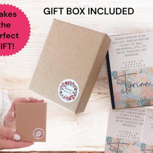 May include: A square brown cardboard gift box with a floral sticker reading Handmade With Love. Inside, a card features the text Turinn meaningful gifts and instructions to remove delicate jewelry before bed or showering and store in a closed container.