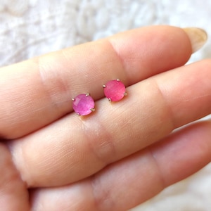 Può includere: Un paio di orecchini a lobo con pietre preziose rosa. Ogni orecchino presenta una gemma rosa rotonda e sfaccettata incastonata in un metallo color argento. Gli orecchini sono esposti su uno sfondo chiaro.