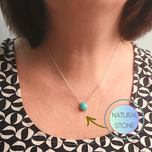 May include: A silver chain necklace with a turquoise teardrop pendant. The pendant is labeled "NATURAL STONE".