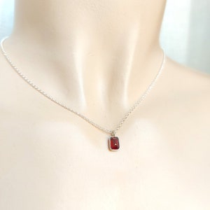 Peut inclure: Un collier en chaîne argent avec un petit pendentif rectangulaire orné d'une pierre rouge.