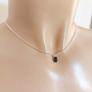 May include: A silver chain necklace with a small, rectangular black gemstone pendant.