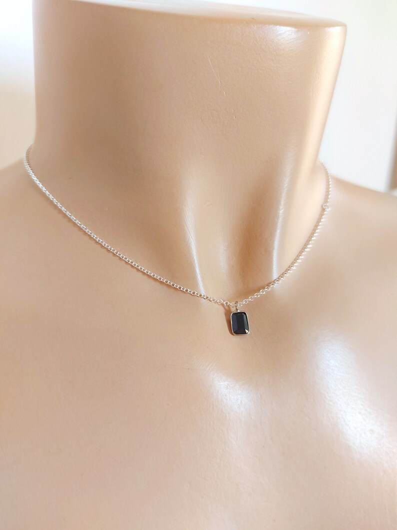 May include: A silver chain necklace with a small, rectangular black gemstone pendant.