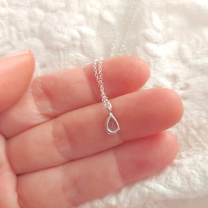 May include: A delicate silver chain necklace with a small teardrop-shaped pendant. The pendant is clear and has a subtle sparkle.