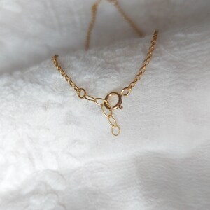 May include: A gold-toned metal chain necklace featuring a circular spring ring clasp mechanism. The delicate link chain includes a short extender section with a small circular loop at the end, designed for adjustable length and secure fastening.