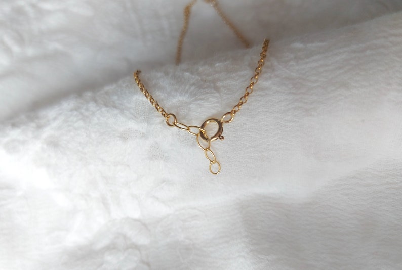 May include: A gold-toned metal chain necklace featuring a circular spring ring clasp mechanism. The delicate link chain includes a short extender section with a small circular loop at the end, designed for adjustable length and secure fastening.