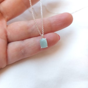Könnte beinhalten: Eine silberne Kettenkette mit einem Anhänger aus hellblauem Edelstein. Der Anhänger hat eine quadratische Form mit abgerundeten Ecken.