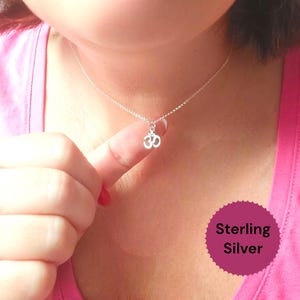 Peut inclure: Un délicat collier en argent sterling avec un petit pendentif symbole Om. Le pendentif est suspendu à une fine chaîne. L'image comprend un haut rose et un autocollant qui dit "Sterling Silver".